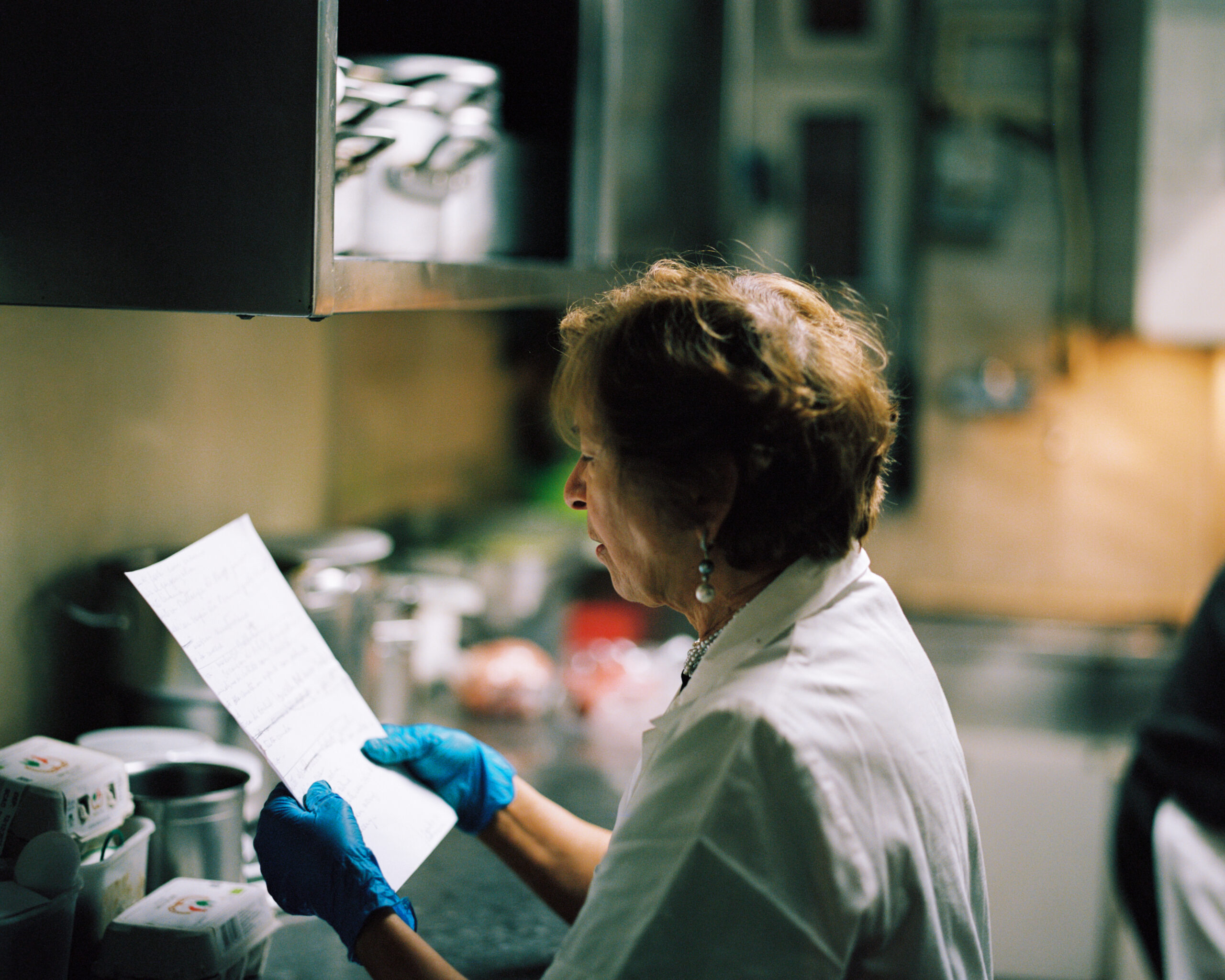 Maria Maggi holds a piece of paper that has a recipe written on it. She is reading the recipe while standing in the kitchen of La Latteria in Milano.