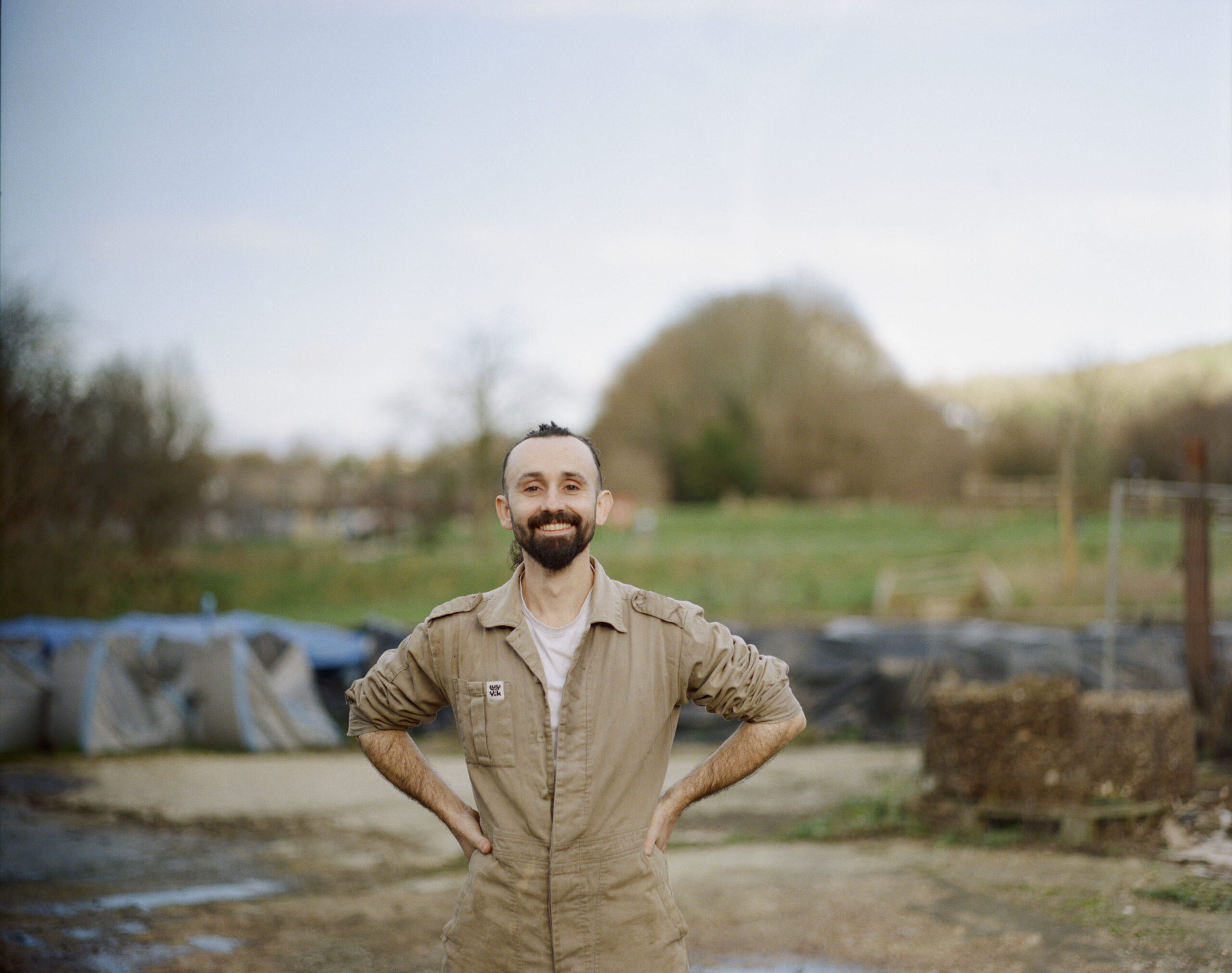 Michael Kennard stands in the middle of the site of his business, Compost Club. Behind him are the trees in a distant park.