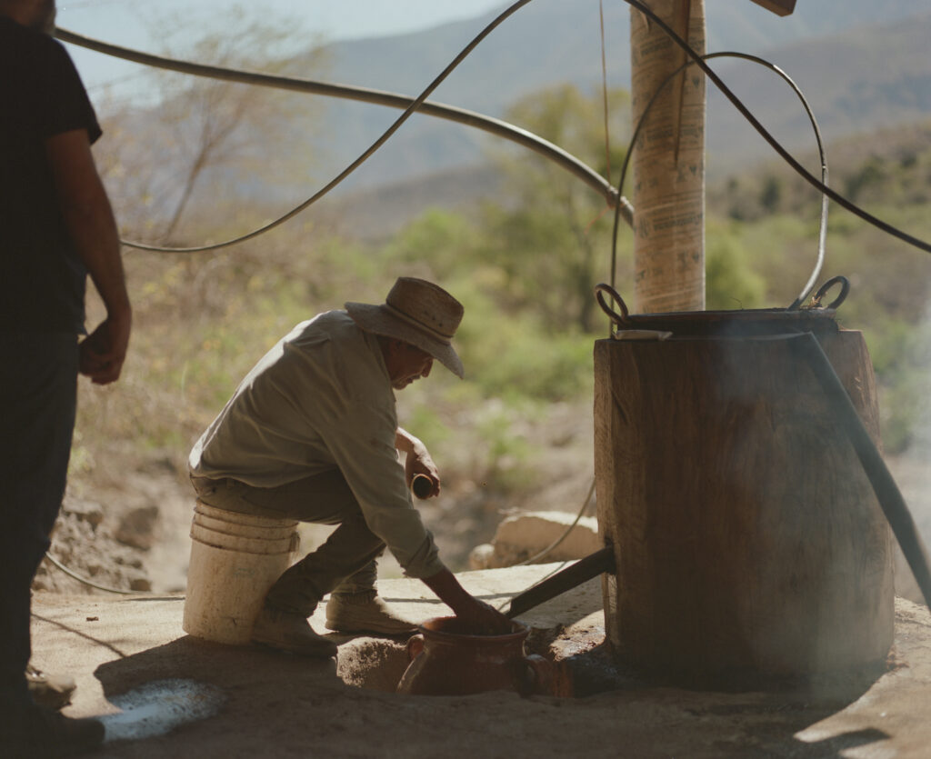 Santos Juárez llena un cuerno de vaca con mezcal que desciende de un alambique de estilo filipinto durante la destilación.