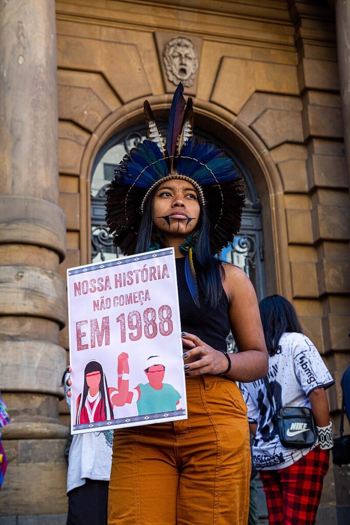 An Indigenous woman, with a traditional headdress, protests against the Marco Temporal thesis in front of the Teatro Municipal in São Paulo.
