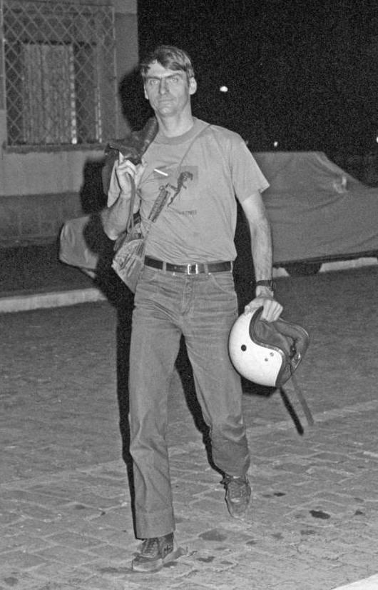 A young Jair Bolsonaro walks while holding a motorcycle helmet and a backpack.