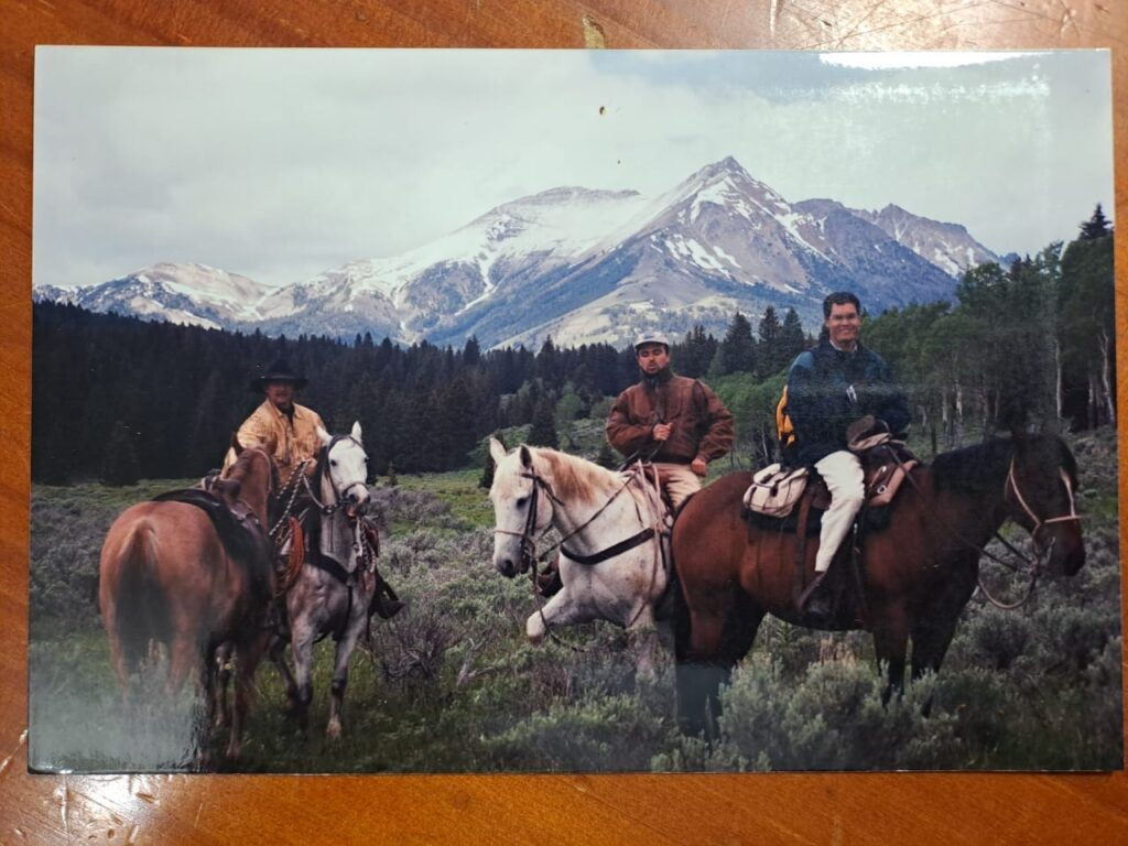 Carlos is seated on a horse, on the right of the photo, with two other men, also on horses. They are all in the Yellowstone National Park.